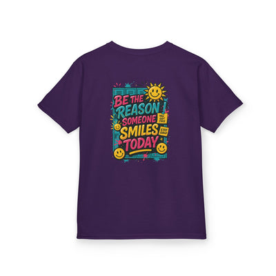 Kids purple motivational t-shirt with 'Be The Reason Someone Smiles Today' graphic and cheerful sun design.