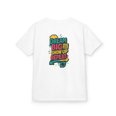 White kids tee featuring 'Dream Big. Show Up. Repeat.' motivational design in vibrant colors.
