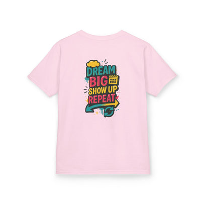 Back view of pink kids tee featuring the message 'Dream Big. Show Up. Repeat.' in colorful bold typography.