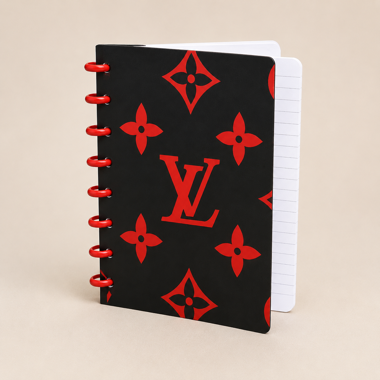 A black spiral-bound notebook with a red Louis Vuitton monogram pattern and red wire binding, shown on a light beige background.
