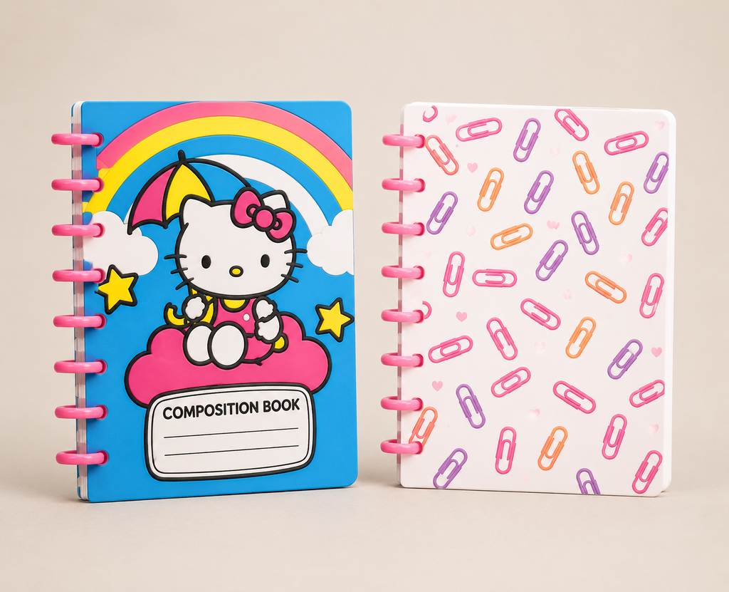 Two spiral-bound composition notebooks with pink wire binding, shown side by side on a light beige background. The left notebook has a blue cover featuring Hello Kitty sitting on a pink cloud under a rainbow, with a blank 'COMPOSITION BOOK' label at the bottom.